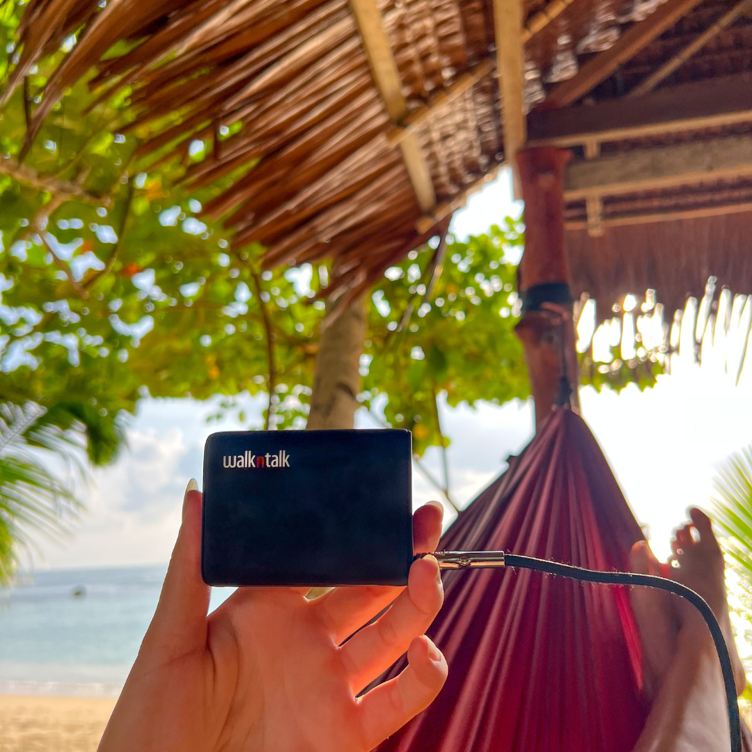 Woman holding a Ultra Powerbank 10000mAh in her hand under a hut on the beach